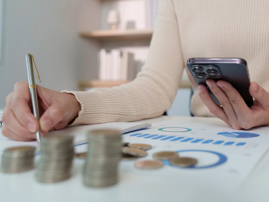 Is 3000 AED a good salary in Dubai. Person using a smartphone and notebook for budgeting representing financial tips for expats in Dubai.